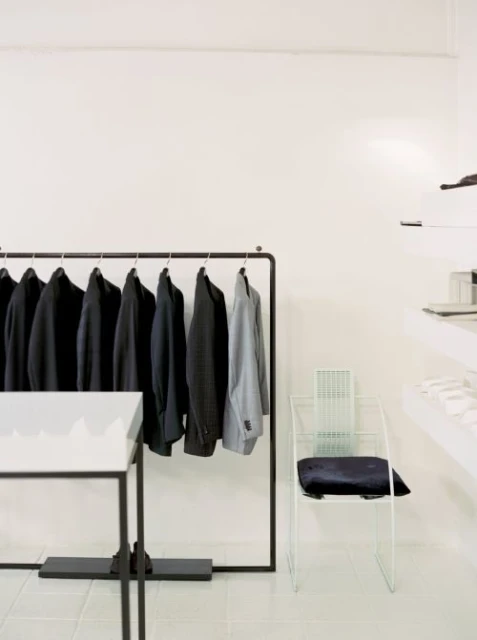 Minimalist clothing store interior with rack of dark jackets, white walls, and light-colored tile floor creating a bright, spacious retail environment.