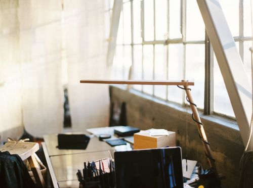 Illuminated wooden desk lamp sits on a desk, shining brightly near a window in a minimalist room, creating a warm, inviting workspace.