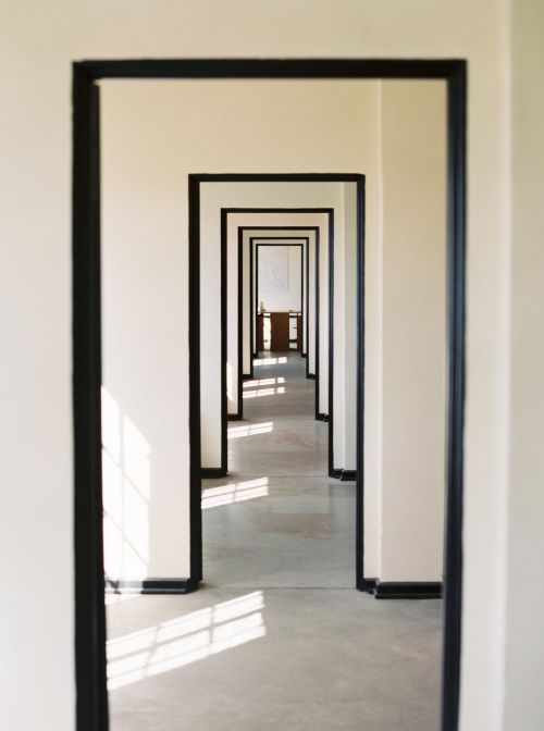 Hallway perspective with repeated doorways receding into the distance, casting geometric light patterns on the floor.