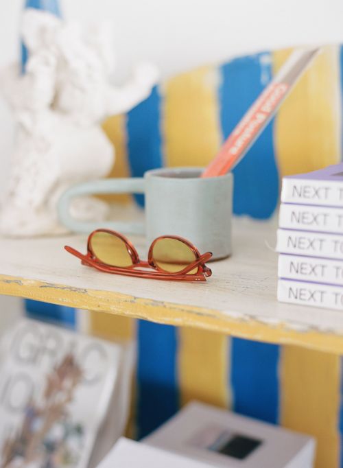 Still life of glasses on shelf with books, a statue, and a mug in a brightly lit indoor setting, showcasing a colorful, artistic composition.