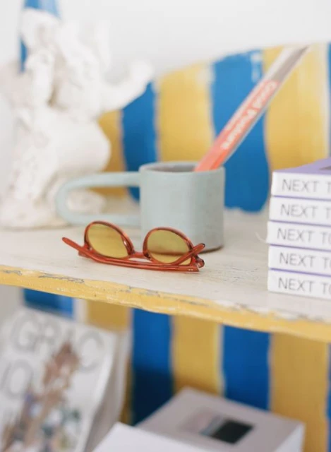 Still life of glasses on shelf with books, a statue, and a mug in a brightly lit indoor setting, showcasing a colorful, artistic composition.
