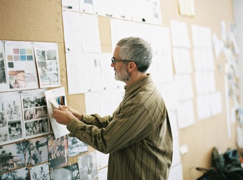 Adult male designer reviews mood board of photos and swatches in a studio with natural light, creating a visual narrative.