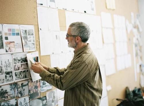 Adult male designer reviews mood board of photos and swatches in a studio with natural light, creating a visual narrative.