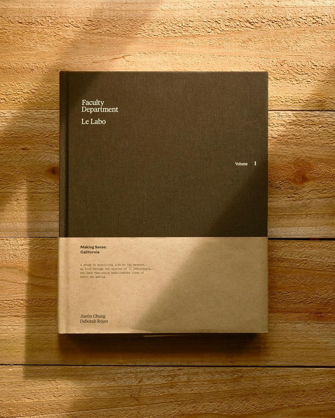 Still life photograph of a hardcover book titled 'Faculty Department Le Labo Volume 1' laying on a wooden plank surface in soft light.