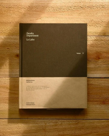 Still life photograph of a hardcover book titled 'Faculty Department Le Labo Volume 1' laying on a wooden plank surface in soft light.