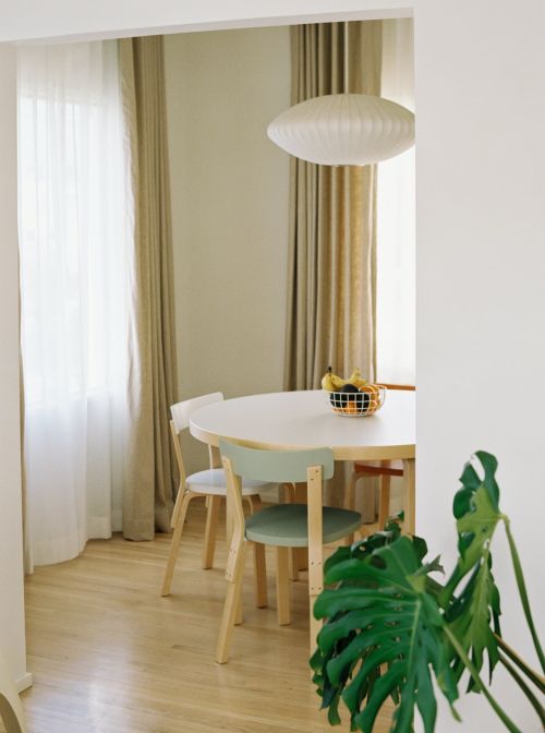 Bright, naturally lit dining room featuring a round white table with pastel chairs, hardwood floors, and a modern pendant light fixture.