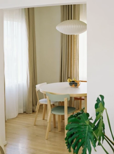 Bright, naturally lit dining room featuring a round white table with pastel chairs, hardwood floors, and a modern pendant light fixture.