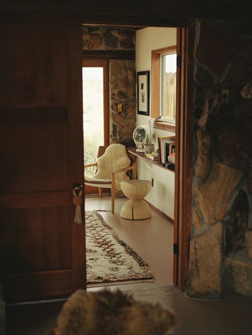 Cozy interior with a wooden chair, stone walls, and an open doorway leading to a bright outdoor space, creating a warm and inviting atmosphere.
