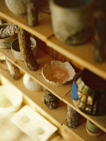Handmade ceramic bowls and vessels displayed on wooden shelves in a home or artist studio with warm lighting and rustic textures.