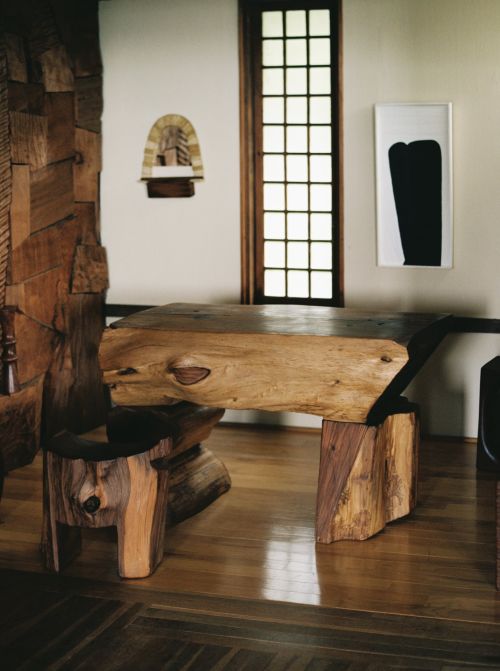 Unique home interior featuring a handcrafted wooden table and chair set with abstract art, set against a bright window and light walls.