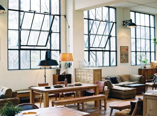 Spacious living area with a large dining table, wooden furniture, and black framed windows that let in natural light.