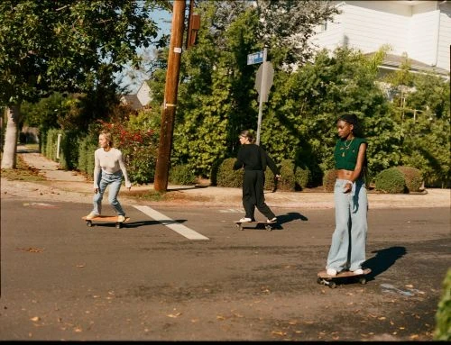 Three young women skateboarding on an asphalt street lined with trees and suburban houses by photographer Justin Chung