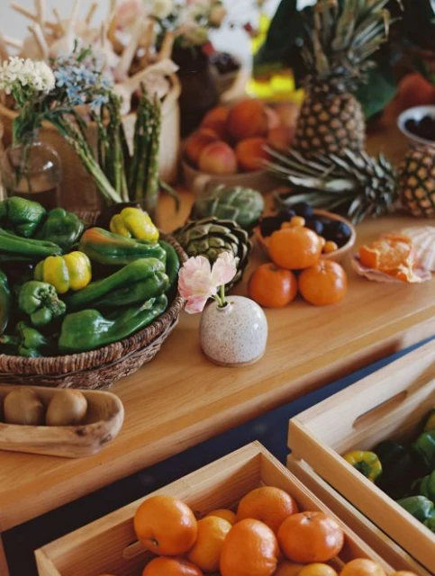 Arrangement of fresh fruits and vegetables on a wooden surface with pineapples, citrus, bell peppers and flowers, indoor still life.