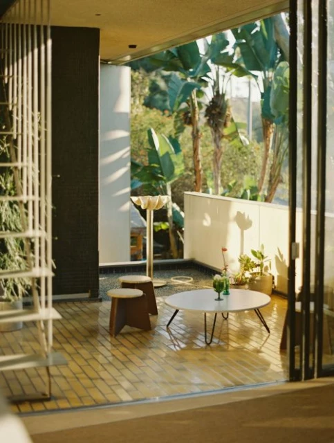 Open-air interior patio with round table, stools, potted plants and lush tropical foliage visible through large open doors.