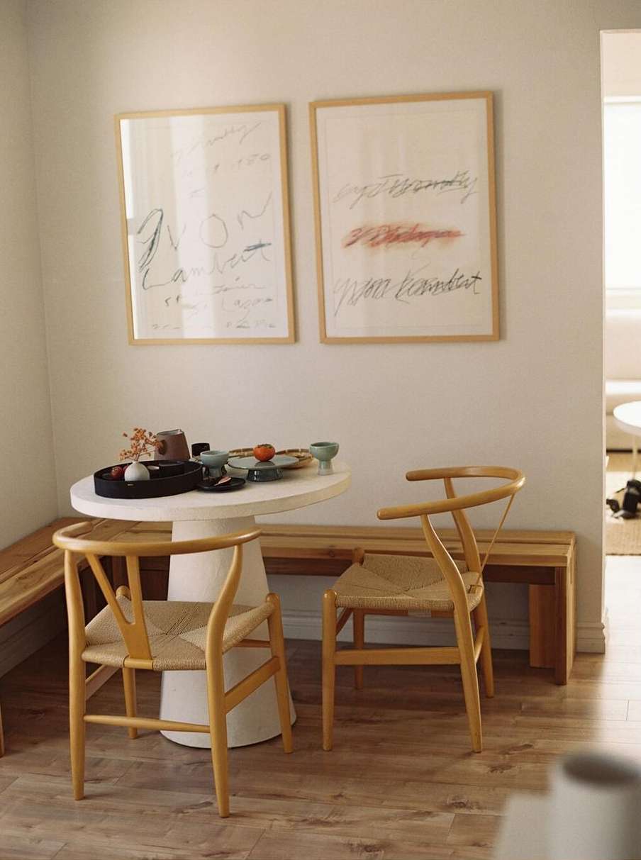 Interior view of a round white table with dishes and light wood chairs, two framed art pieces hang on the wall. 
