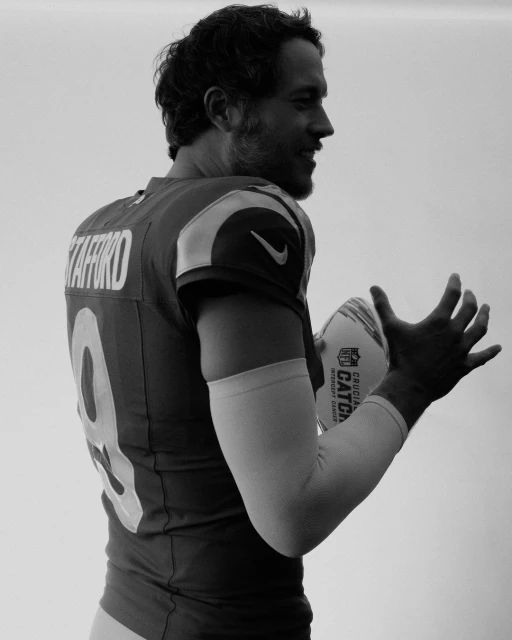 Black and white portrait of football player in uniform holding a football. A close-up view captures the athlete indoors.