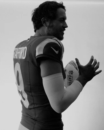 Black and white portrait of football player in uniform holding a football. A close-up view captures the athlete indoors.