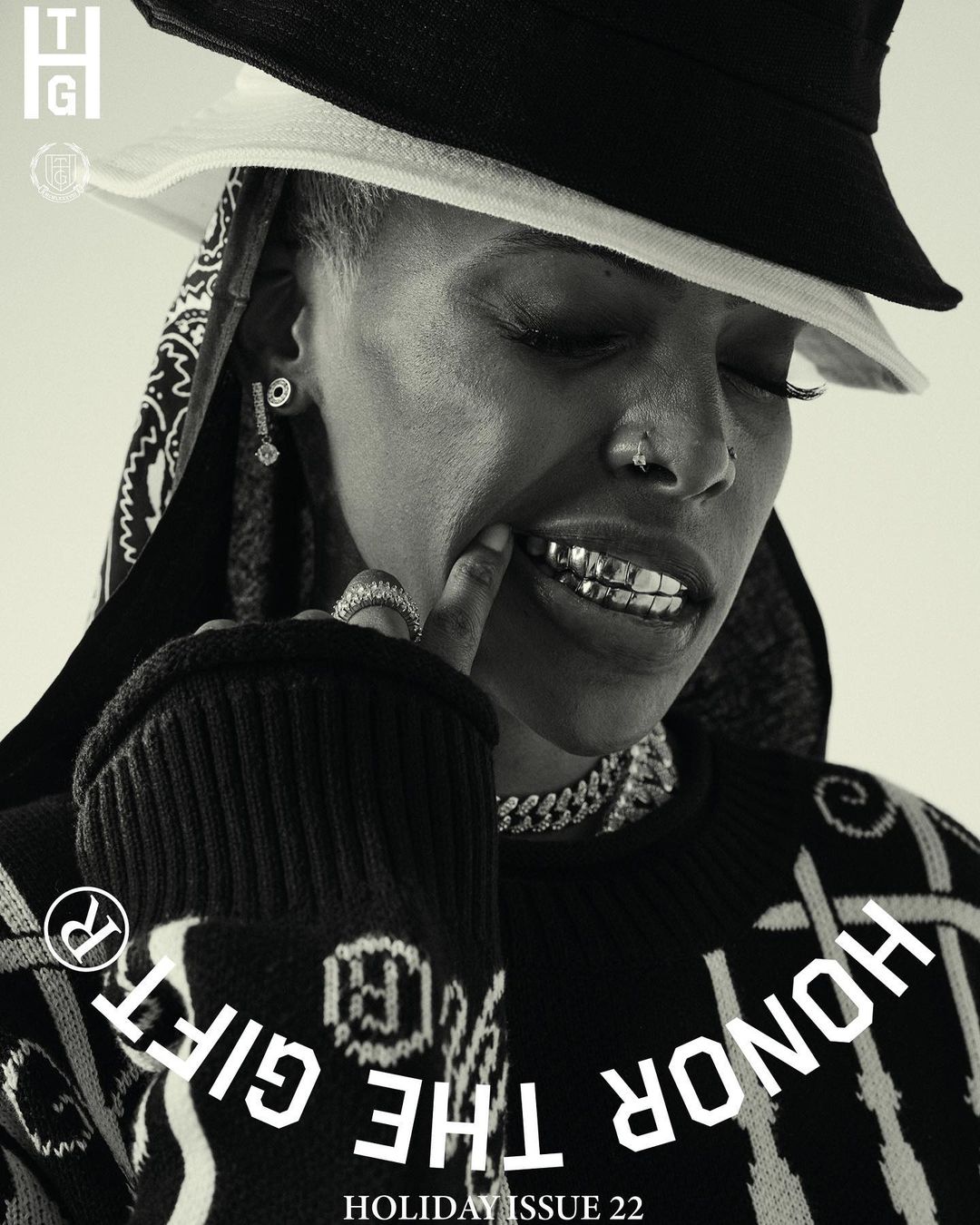 Black-and-white fashion portrait: African-American woman with grill and bucket hat. Silver jewelry and a patterned sweater complete the look.