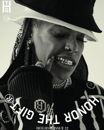 Black-and-white fashion portrait: African-American woman with grill and bucket hat. Silver jewelry and a patterned sweater complete the look.