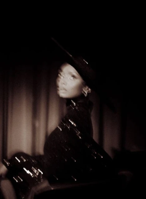 Portrait of a stylish African American woman in a black hat and turtleneck dress with light bokeh effect in a dark, moody ambiance.