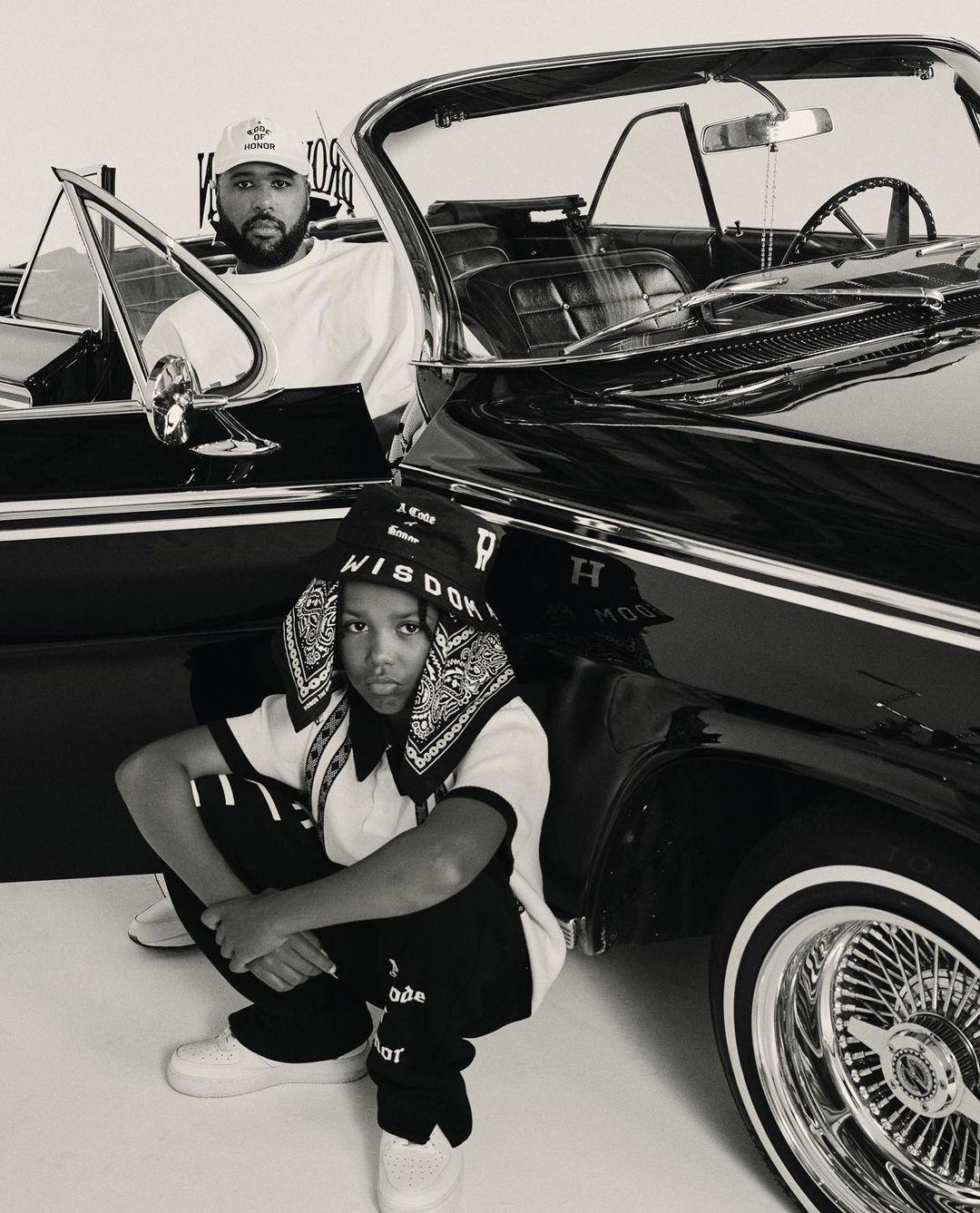 Monochrome portrait by Mark Clennon featuring a man seated in a vintage convertible and a child crouching in the foreground.