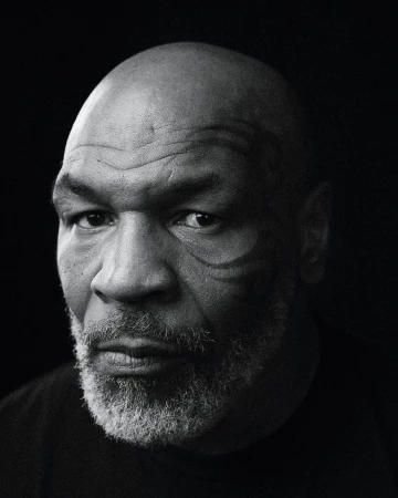 Black and white portrait of adult male with bald head and distinctive face tattoo on black background looking towards camera.