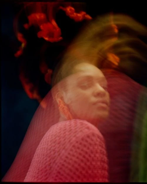 Portrait of a Black woman with blurred motion effect in red top against dark background with red and orange light flares.