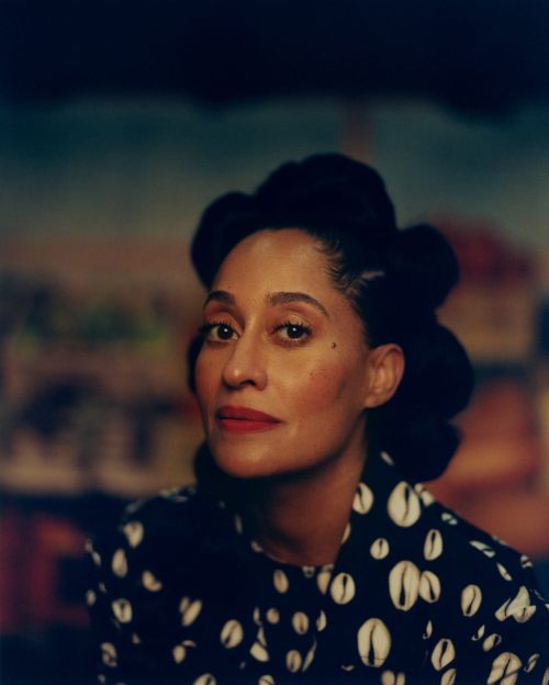 Close-up portrait of an adult woman with dark hair styled up, wearing a patterned top against a blurred painted backdrop.