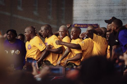 Enthusiastic group of African American men in yellow shirts celebrate together, captured with a dynamic, slightly grainy aesthetic.