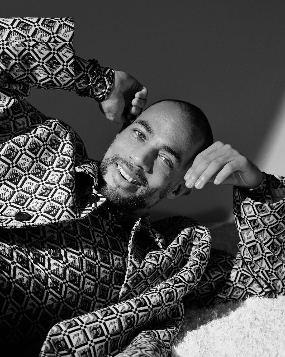 Black and white portrait of an African American adult male with a light beard, smiling while laying down in a patterned shirt.