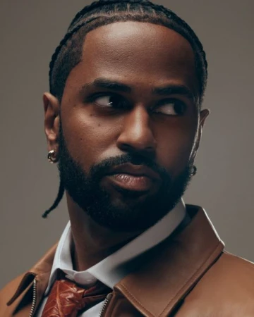 Portrait of Big Sean with braided hair wearing a tan leather jacket, white shirt, and patterned tie against a grey background