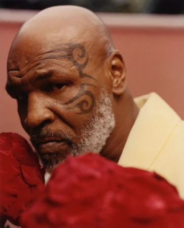 Close-up of Mike Tyson with a tribal face tattoo and red boxing gloves, captured in a portrait, conveying strength and determination.