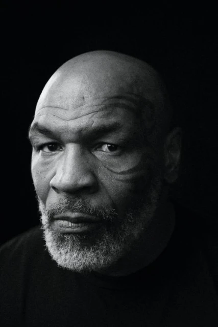 Black and white close-up portrait of a bald adult male with a gray beard and face tattoos against a solid dark background.