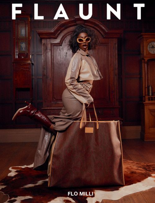 Fashion editorial shot featuring a Black woman in a coordinated outfit, posing with a large tote bag in an indoor setting against wooden furniture.