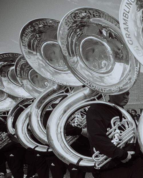 A row of tuba players in uniform, holding their instruments. The tubas feature text that reads GRAMBLING STATE UNIVERSITY WORLD FAMOUS.
