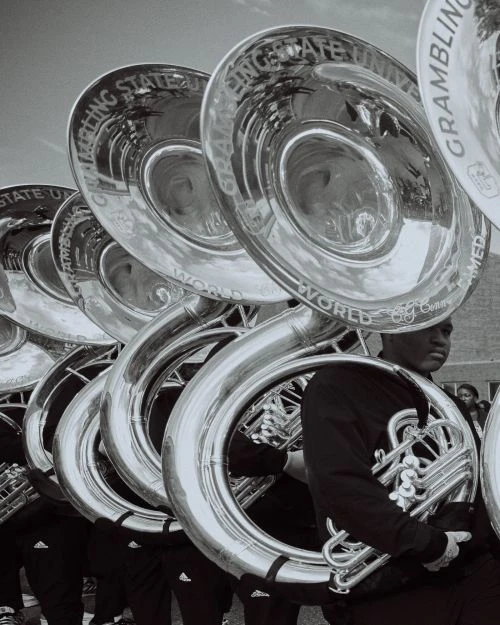 A row of tuba players in uniform, holding their instruments. The tubas feature text that reads GRAMBLING STATE UNIVERSITY WORLD FAMOUS.
