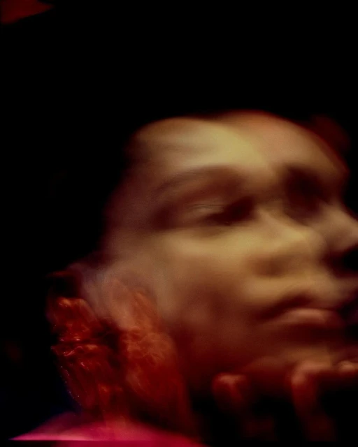 Portrait of a person with blurred features in warm tones against a dark background, creating an abstract and dreamy effect.
