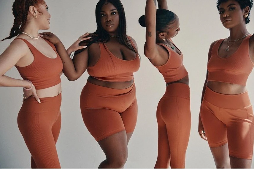 Group portrait of four multi-ethnic adult female models wearing matching rust-colored workout crop tops and leggings or bike shorts against a neutral backdrop.