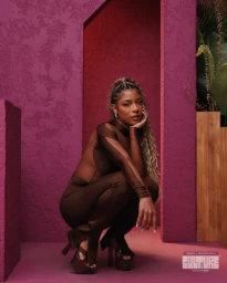Woman in brown sheer cutout jumpsuit posing against a textured fuchsia pink wall and matching floor