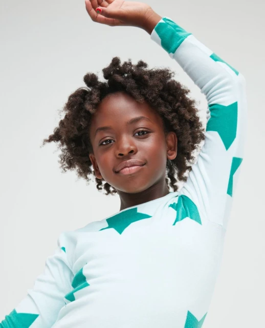 Portrait of a smiling Black child with curly hair, wearing a star-patterned shirt against a neutral background, looking at the camera.