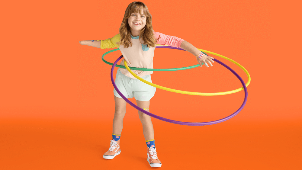 Smiling child hula hooping with colorful hoops against an orange backdrop, captured in a vibrant and playful studio shot.