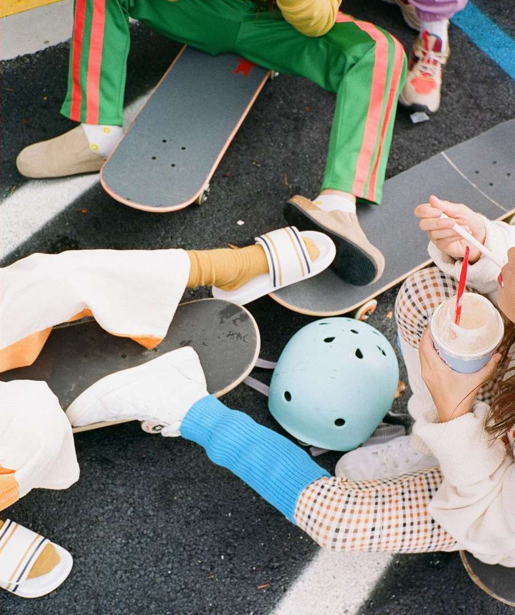 Overhead shot of a group of people sitting on skateboards outdoors. Some are drinking from cups with straws in them.