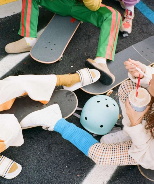 Overhead shot of a group of people sitting on skateboards outdoors. Some are drinking from cups with straws in them.