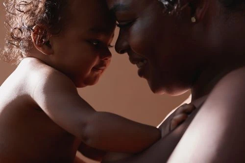 Close-up of a baby and an adult touching foreheads; the baby is on the left and the adult is on the right; warm, soft light.