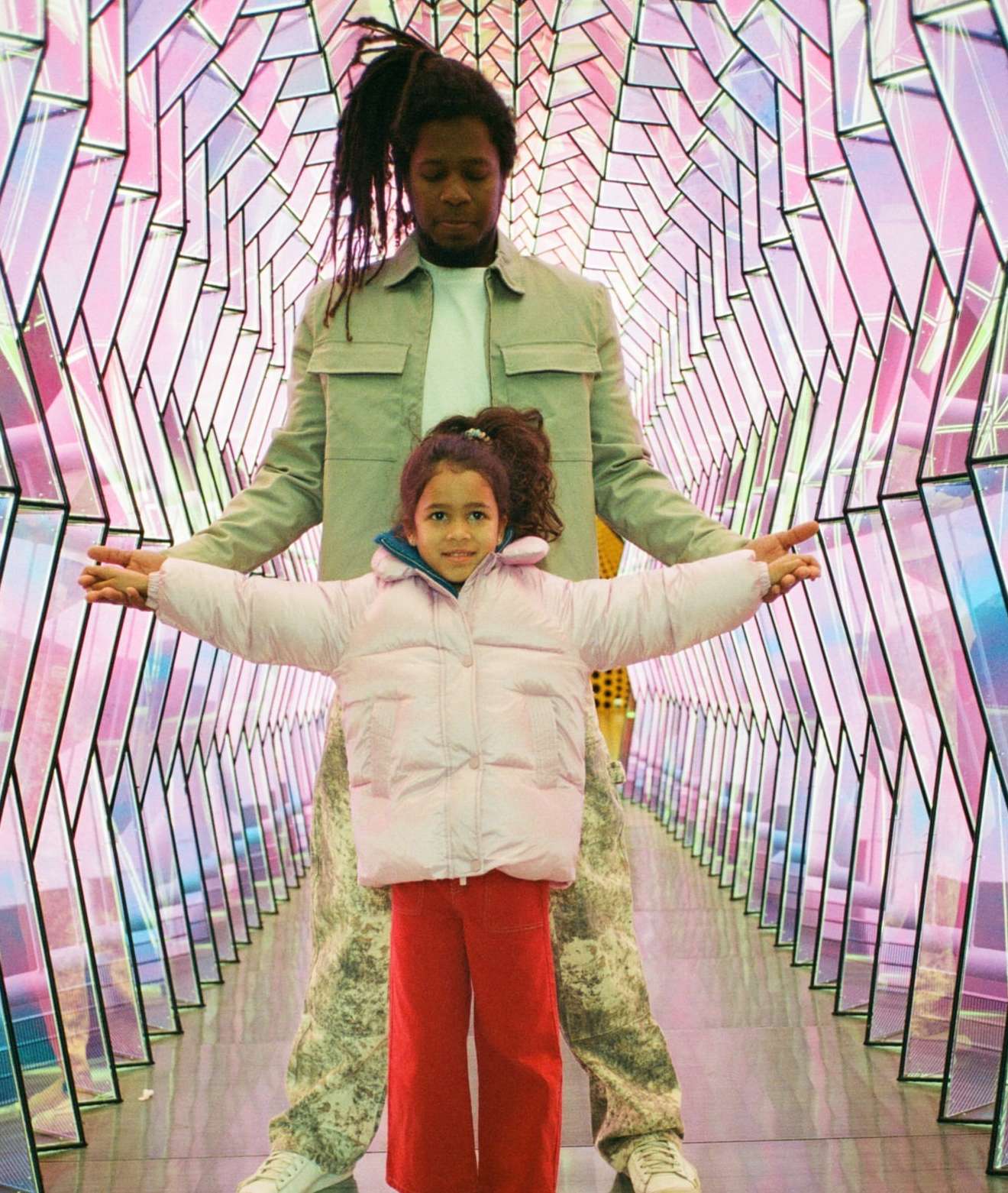 Adult and child pose in an art installation. The installation features angled geometric shapes with iridescent lighting, creating a modern art piece.