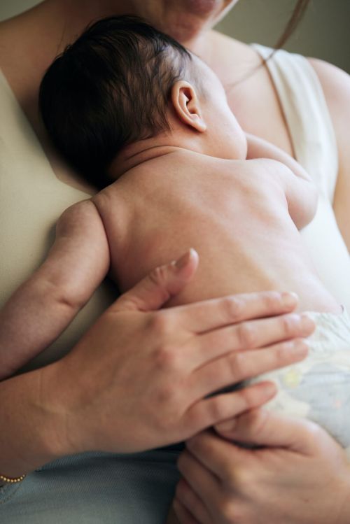 Close-up of a newborn baby lying on an adult's chest. The baby is facing away from the camera, and the adult's arms are around the baby.