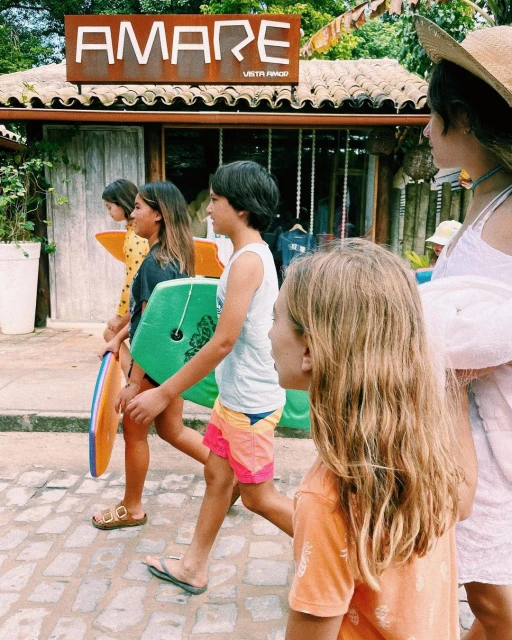 Group of children walking near the beach with bodyboards, dressed in casual summer clothing and sandals, captured in natural lighting.
