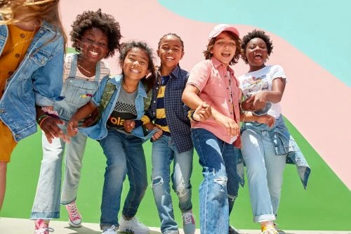 Group of smiling multi-ethnic kids standing outdoors in casual clothes against an abstract colorful background, showcasing youthful fashion.