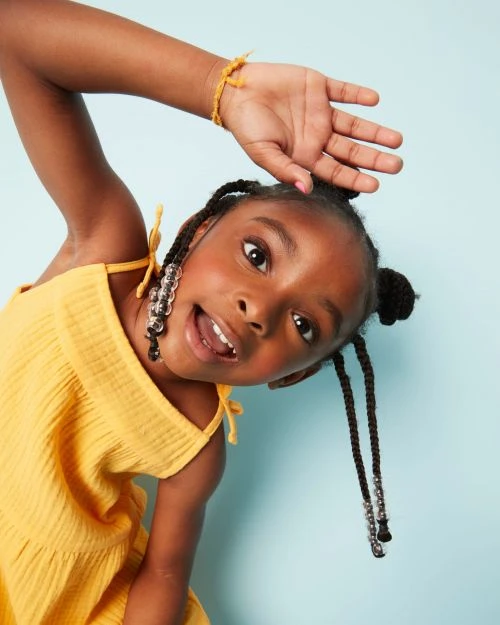 Adorable young girl with braided hair and a yellow dress smiles against a blue background, showcasing a happy and youthful portrait.