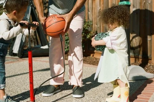 Two children and an adult with a basketball and a pump in an outdoor setting, capturing a playful family moment.